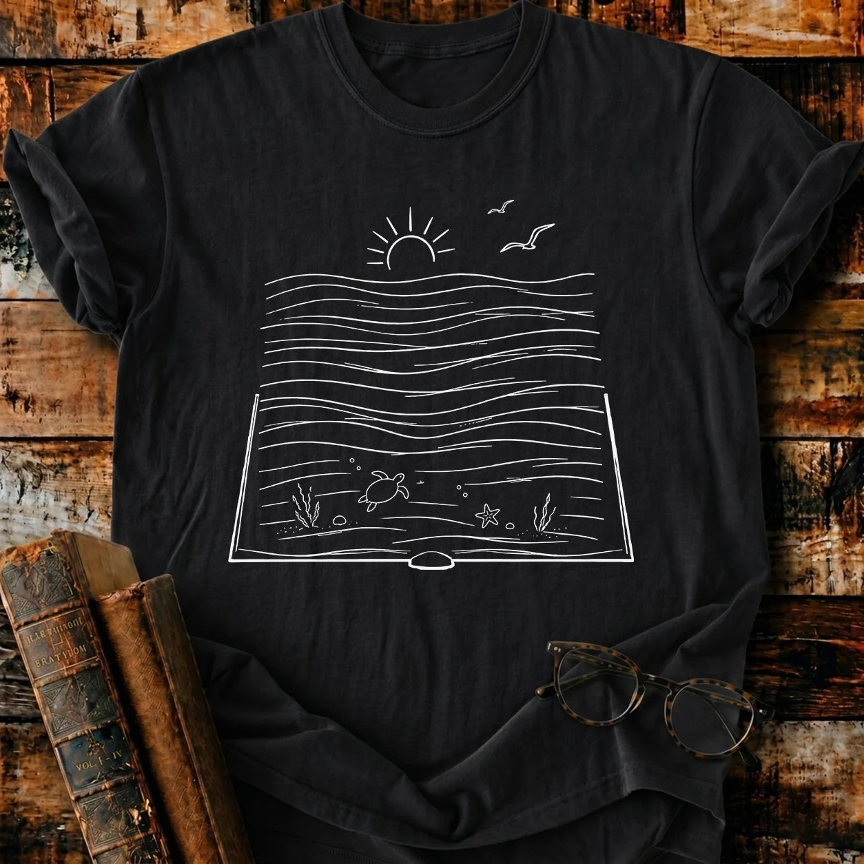Black Comfort Colors t-shirt with a white line art design of an open book revealing an ocean scene.