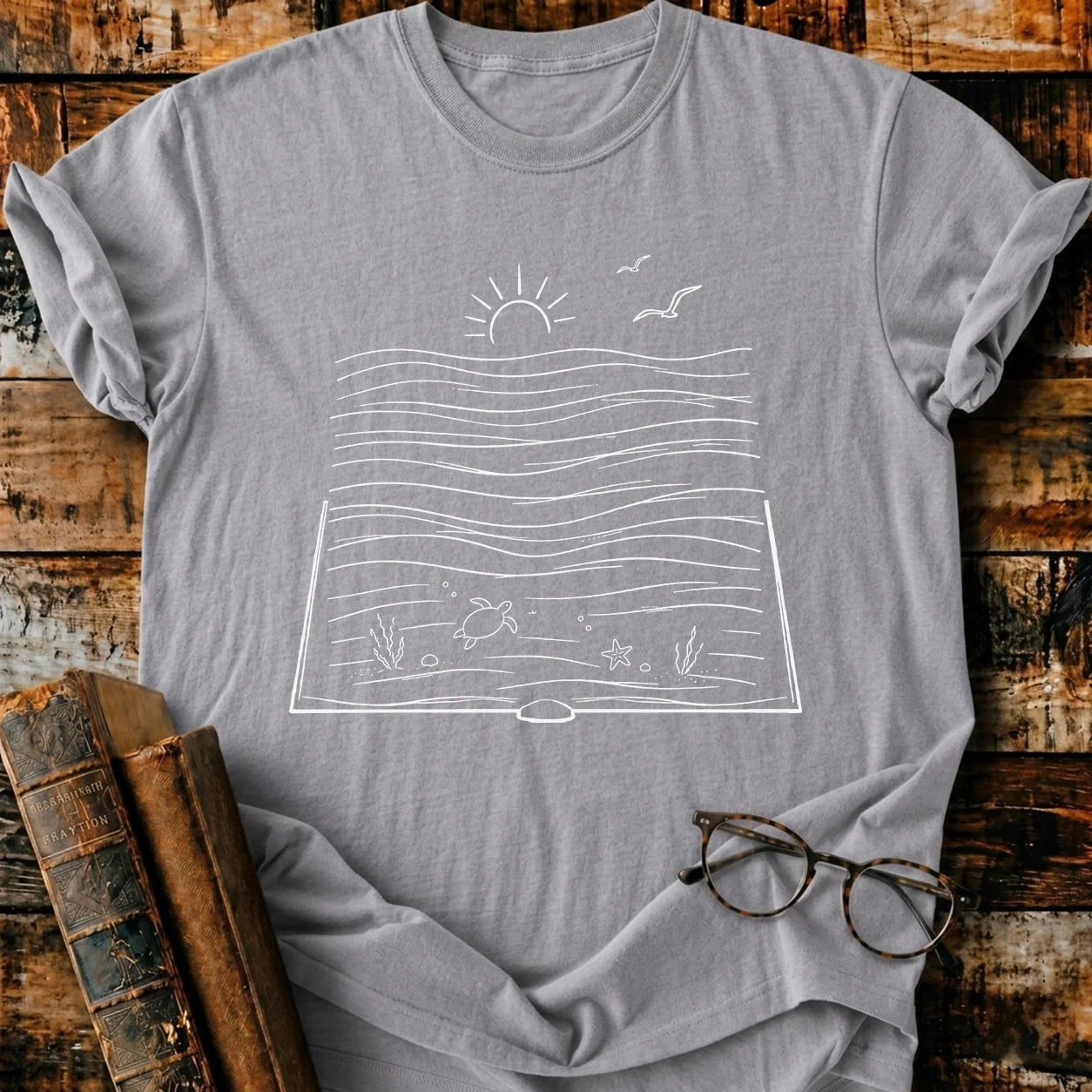 Gray Comfort Colors t-shirt with a white line art design of an open book revealing an ocean scene.