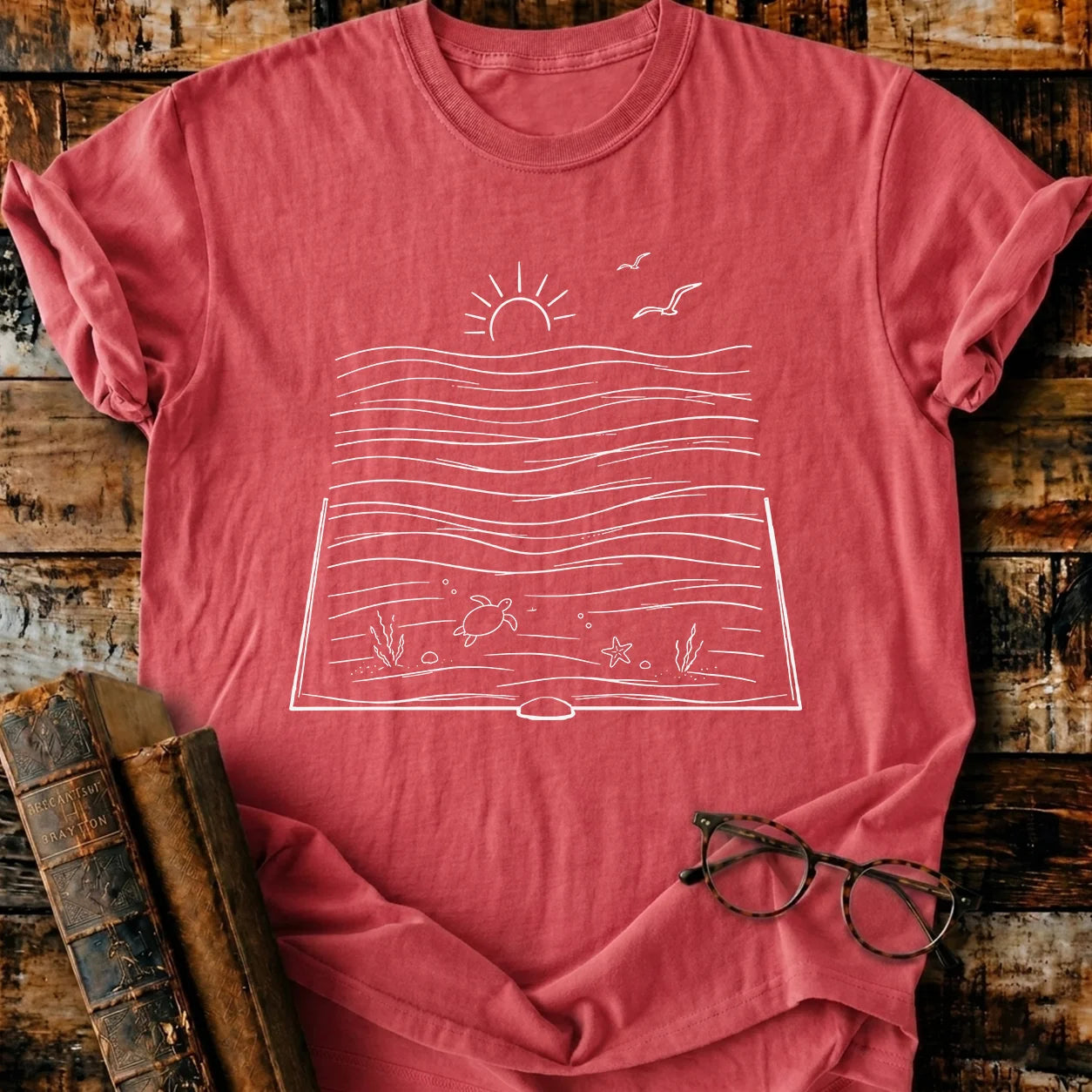 Red Comfort Colors t-shirt with a white bookish ocean graphic, featuring a sun, waves, turtle, and seagulls.